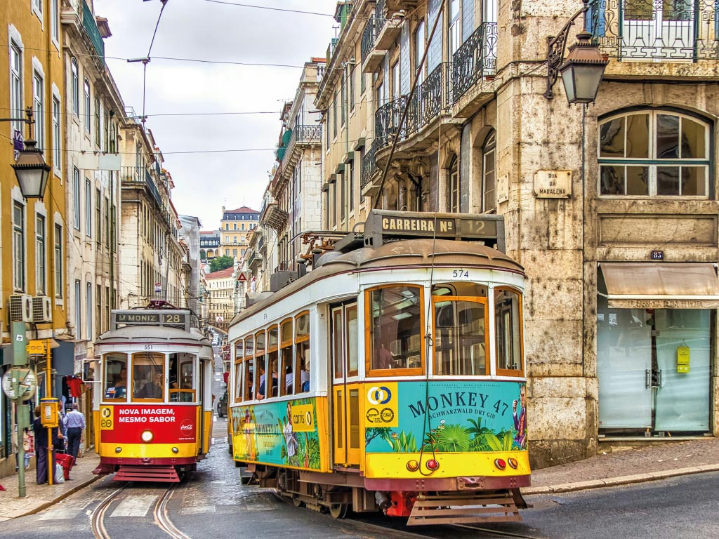 Two traditional trams cross paths on a historic Lisbon street, illustrating the news headline: Portugal as the best destination in Europe 2025.